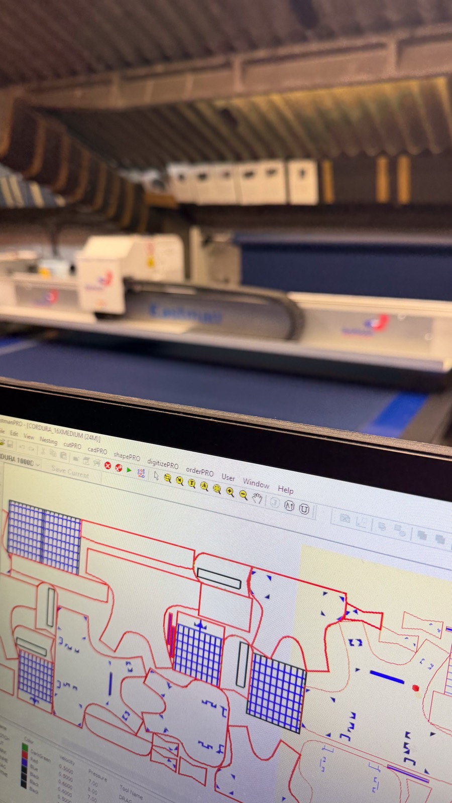 Automated cutting table in the Glasgow factory — CAD-nested Cordura patterns on screen, cutter behind